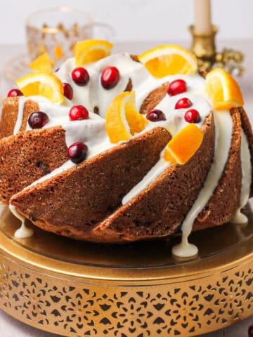 Glazed cranberry sour cream Bundt cake, sitting on a gold cake stand with candles and cranberries scattered throughout the foreground.