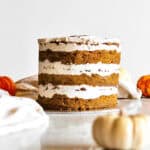 Pumpkin chai cake, sitting on a cake plate, surrounded by small pumpkins in the foreground and background.