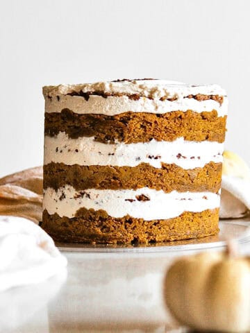 Pumpkin chai cake, sitting on a cake plate, surrounded by small pumpkins in the foreground and background.
