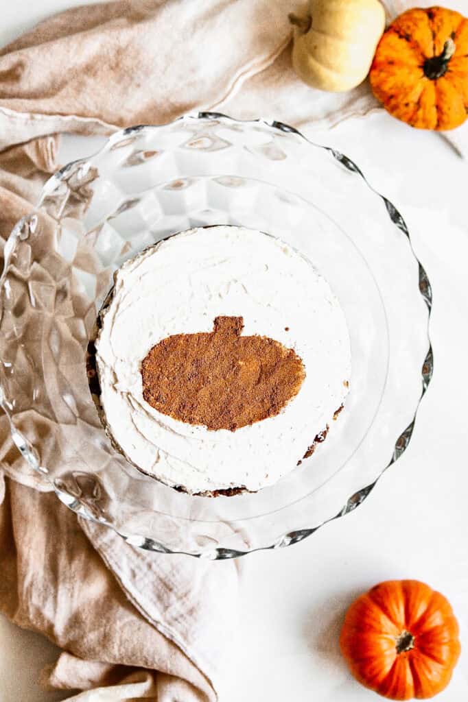 Pumpkin chai cake slice on glass plate with pumpkins around it.