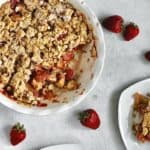 image of baked strawberry apple crumble alongside two small plates of individual servings