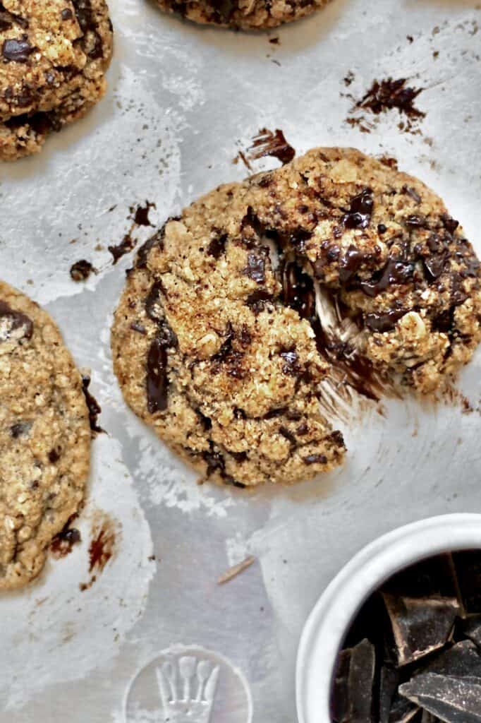 up-close image of a baked Oat Flour Chocolate Chip Cookie, with other cookies on the edges of the frame and a small bowl of chocolate chunks off to the side