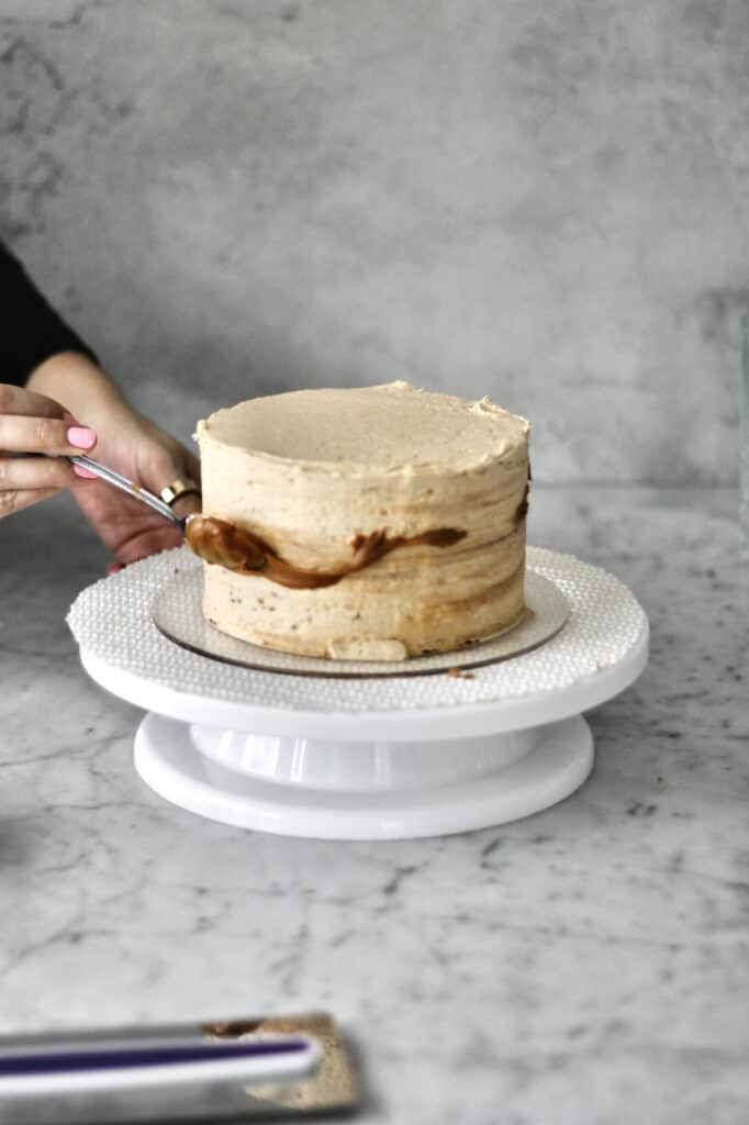 smoothing out the Biscoff buttercream on the cake and adding a marbling design with melted Lotus Biscoff spread