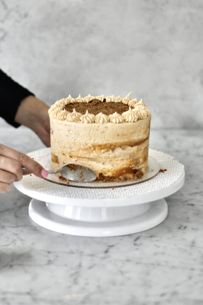 pressing baked Biscoff cake crumbs into side of cake with a spoon