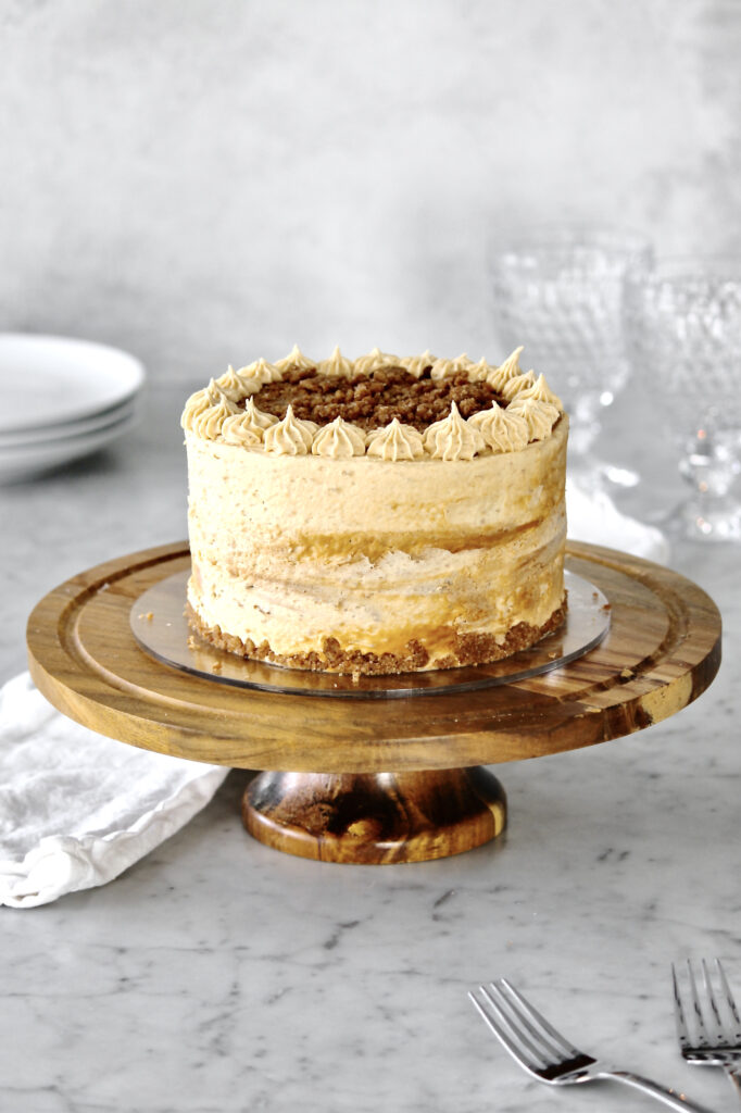 Lotus Biscoff cake on a brown wooden cake stand with glasses, plates, and silverware also in the scene