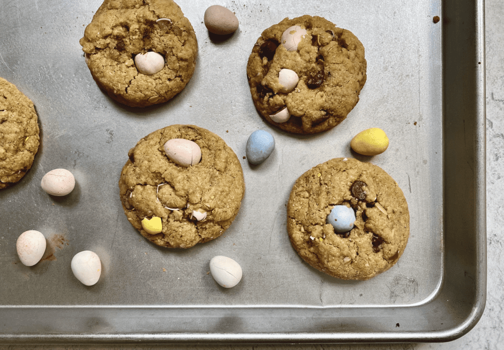 Easter chocolate chip cookies, with mini Cadbury eggs and chocolate chips scattered throughout 5 baked cookies on an aluminum baking sheet