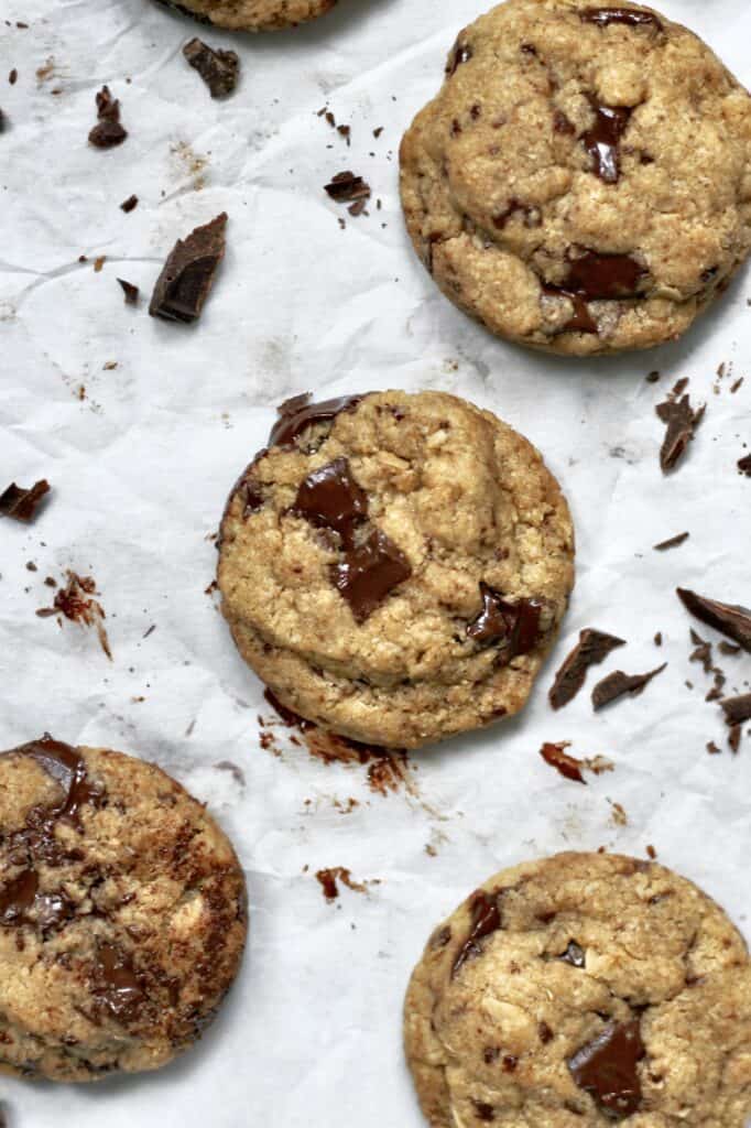 big batch chocolate chip cookies on a baking sheet with white parchment paper underneath, surrounded by pieces of chocolate
