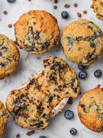 Overhead view of blueberry chocolate chip muffins, surrounded by small blueberries and mini chocolate chips.