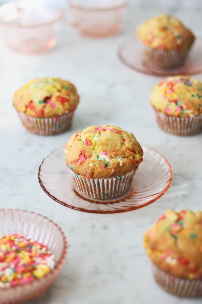 image of baked birthday cake muffins, sitting on pink plates on a grey countertop