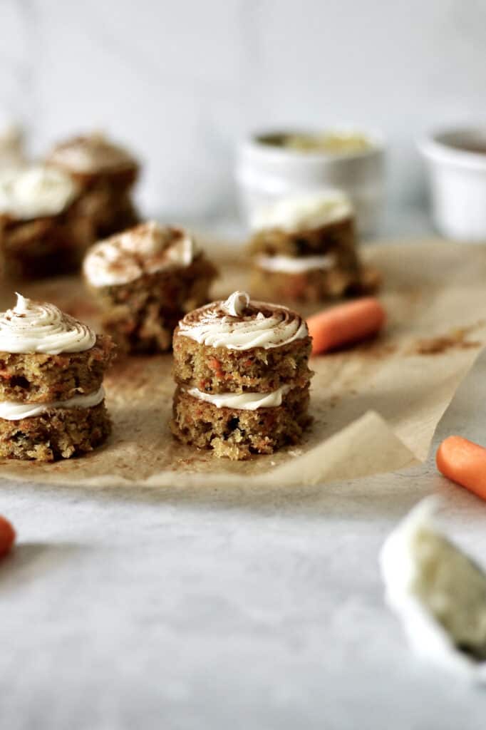 bite-sized layered carrot cake, sitting on a brown piece of parchment paper, dusted with ground cinnamon