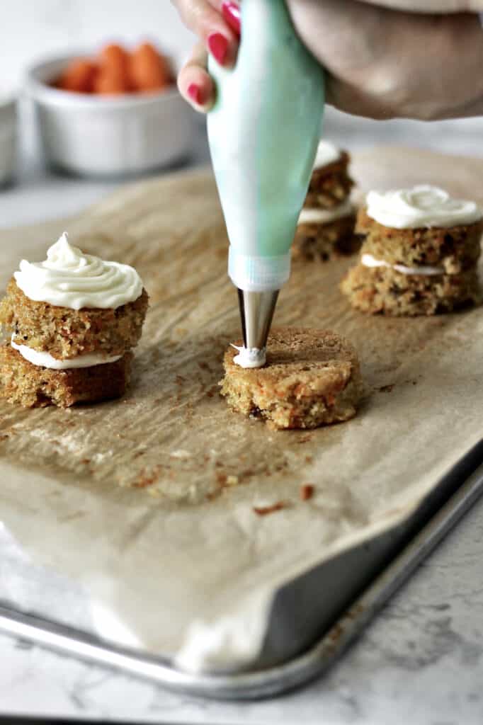 action shot of blue piping bag adding cream cheese frosting to mini carrot cakes