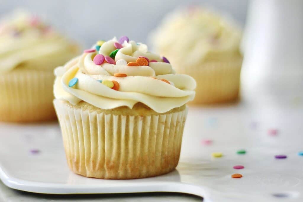 three vanilla cupcakes on a white platter with one up close in the center of the shot