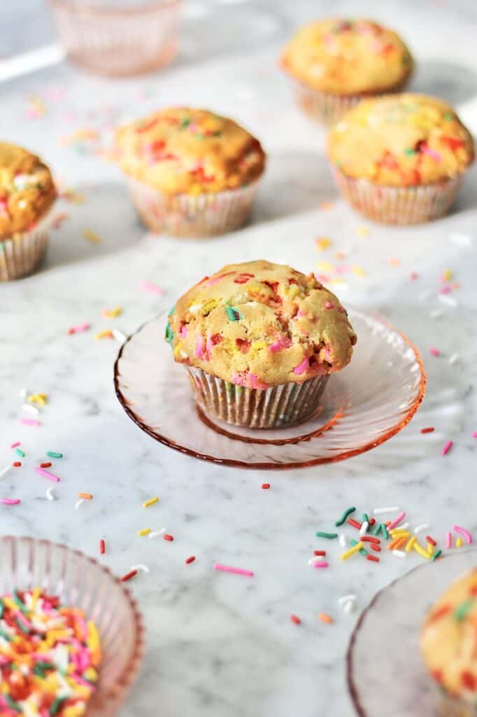 funfetti muffins sitting on light pink plates, surrounded by colorful sprinkles