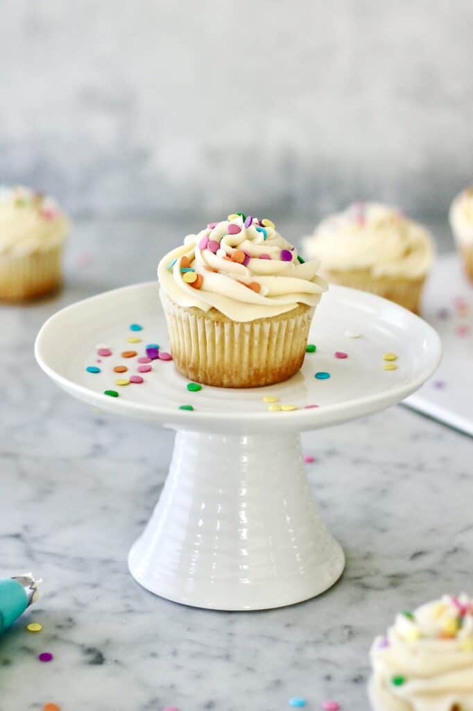 vanilla cupcake on a white stand, surrounded by lots of confetti sprinkles