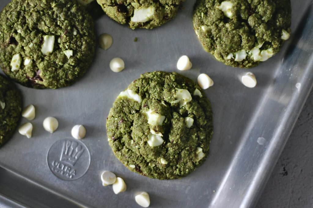 baked green cookies, still on the baking sheet, with white chocolate chips surrounding them