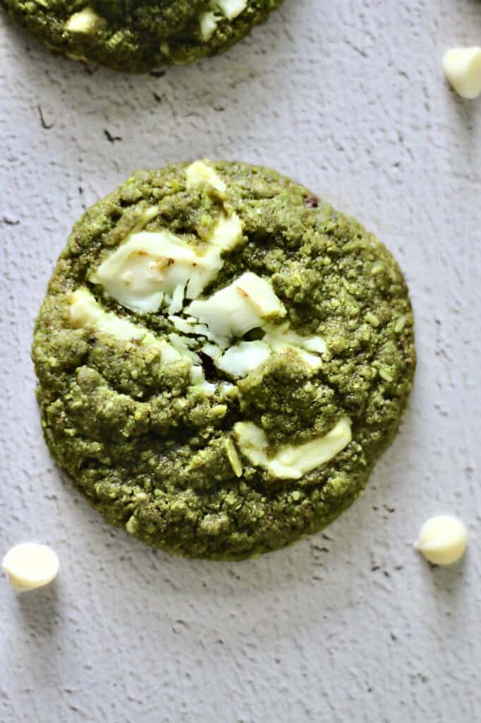 up-close image of a matcha cookie, with white chocolate chunks baked into it and chips surrounding it
