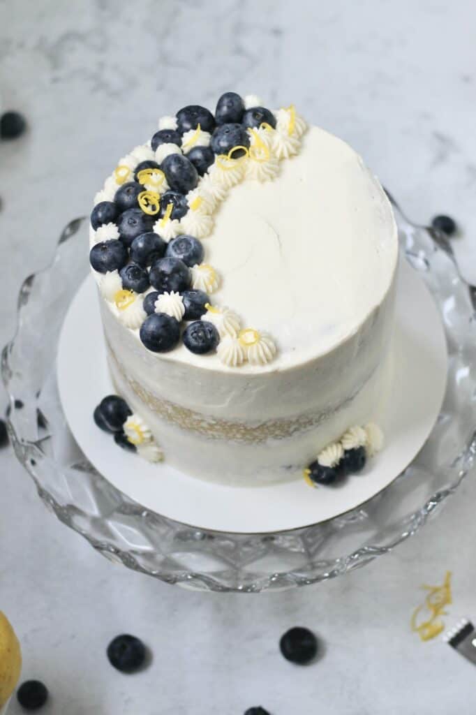 overhead shot of a lemon berry mascarpone cake sitting on a glass cakestand, with lemons and berries scattered around it