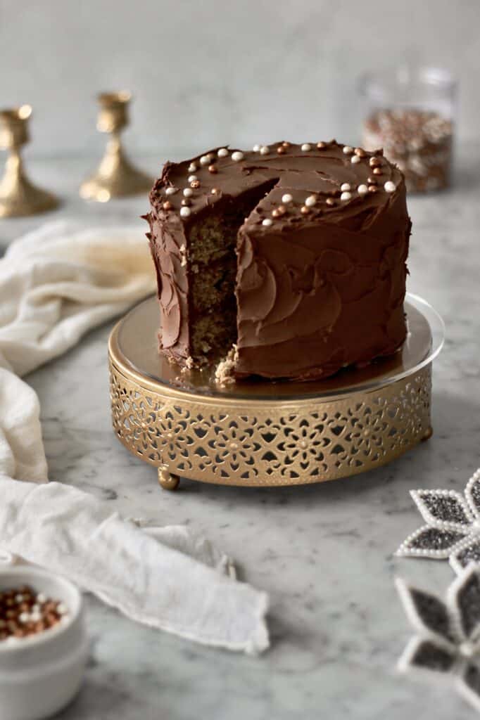 up-close image of banana cake with chocolate frosting, sitting on a short gold cake stand, with a look at the inside due to a slice being removed