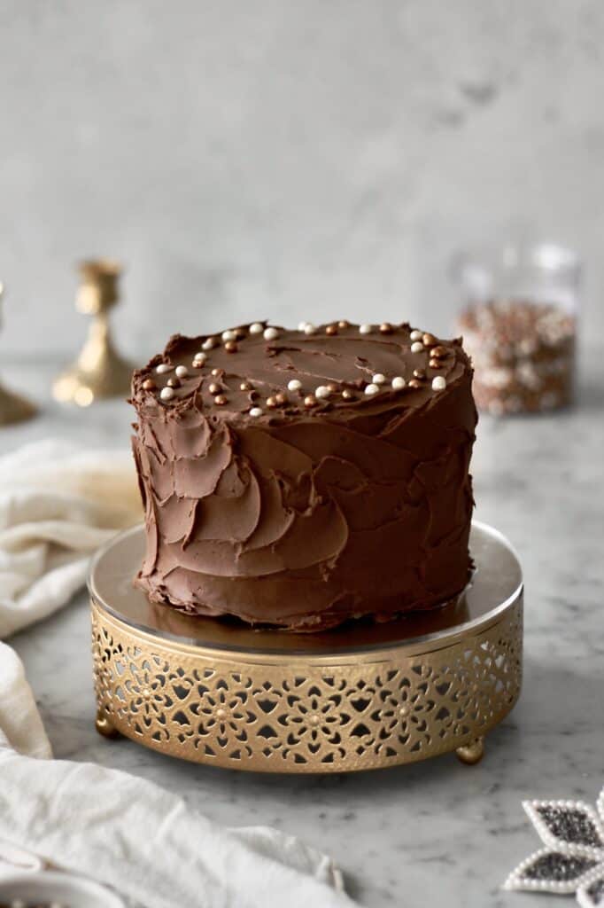 up-close image of banana cake with chocolate frosting, sitting on a short gold cake stand