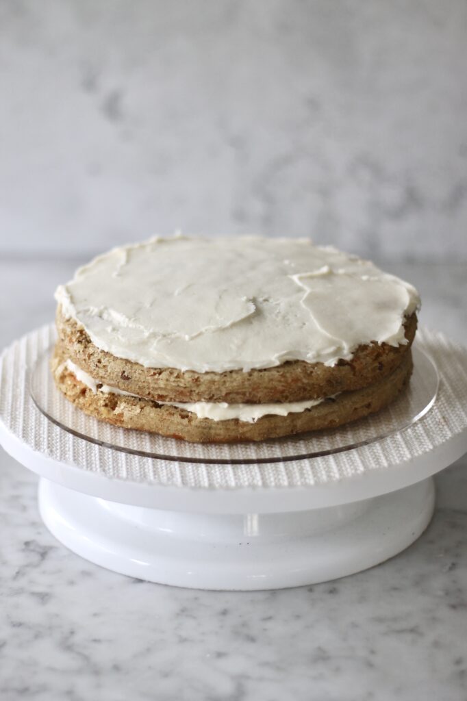 two of three layers of carrot cake sitting on a white cake turntable