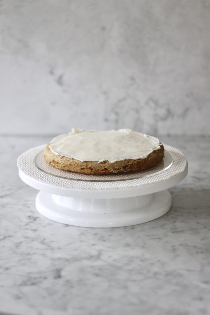 first of three layers of carrot cake sitting on a white cake turntable