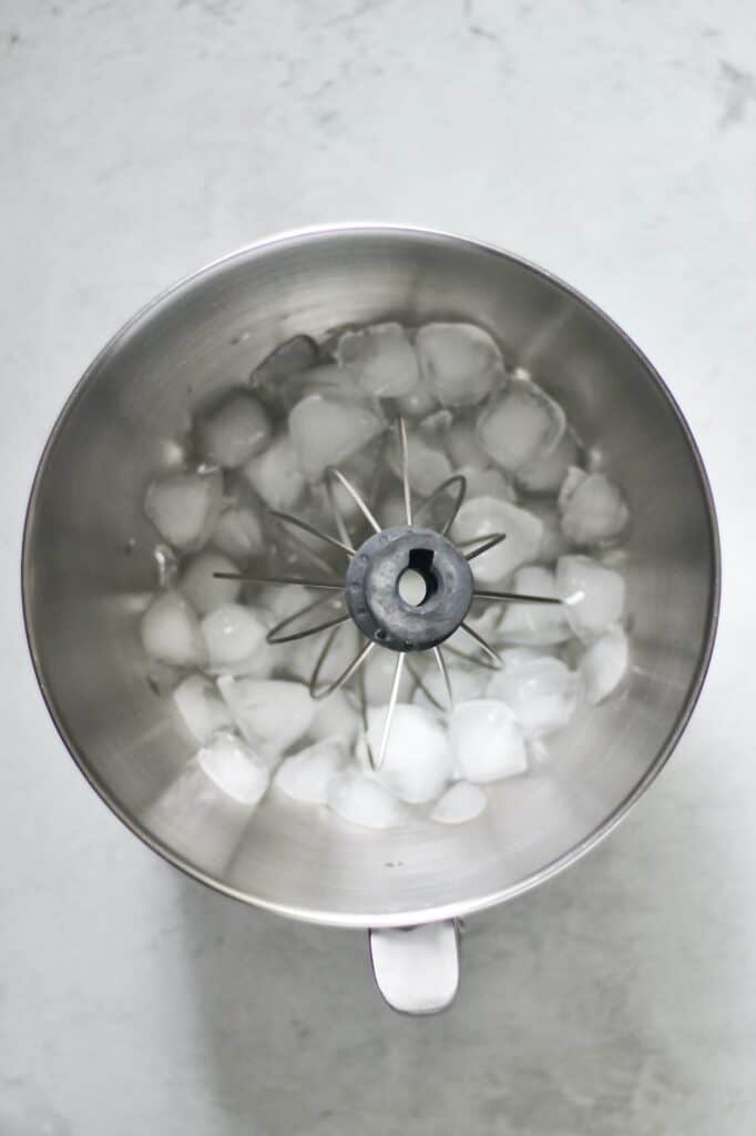 overhead image of a mixing bowl, chilled with ice, as a whisk attachment sits within it