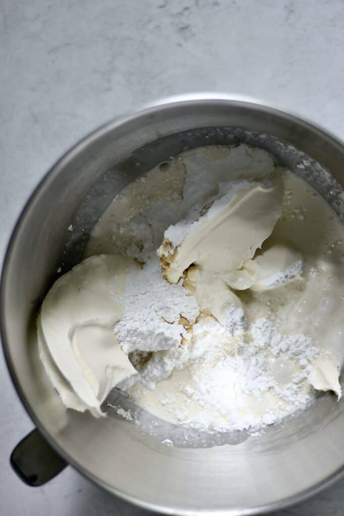 bowl of ingredients for mascarpone cheesecake recipe, including powdered sugar, heavy cream, and mascarpone, unmixed