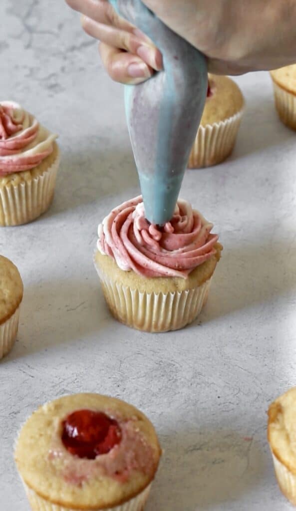 piping strawberry frosting onto cupcake