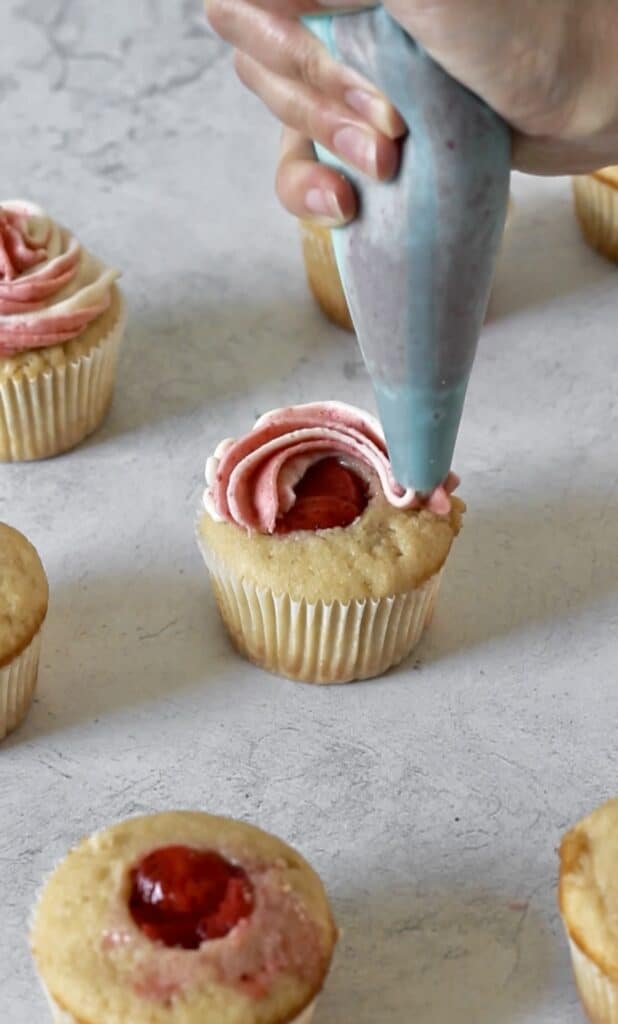 piping strawberry frosting around cupcake filling