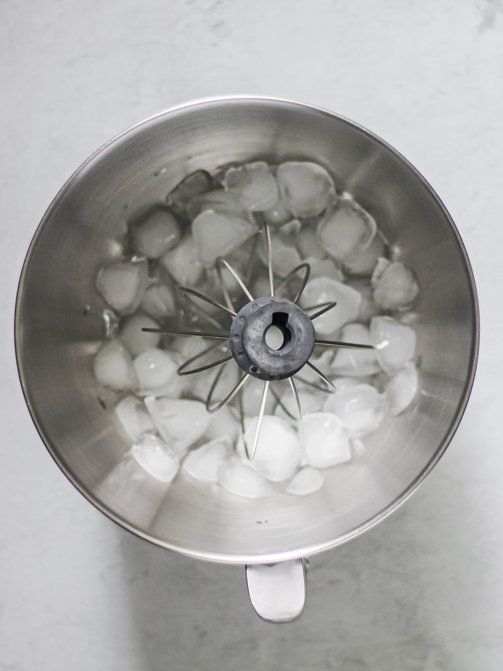 Overhead image of a mixing bowl, chilled with ice, as a whisk attachment sits within it.
