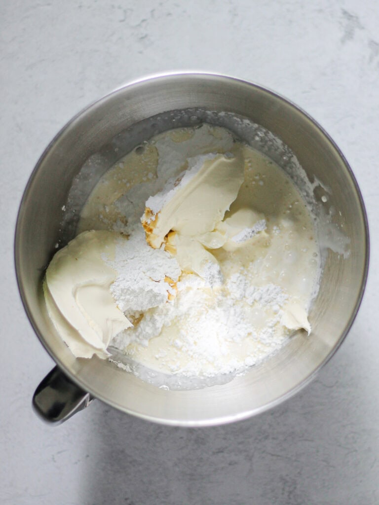 Bowl of ingredients for mascarpone cheesecake recipe, including powdered sugar, heavy cream, and mascarpone, unmixed.