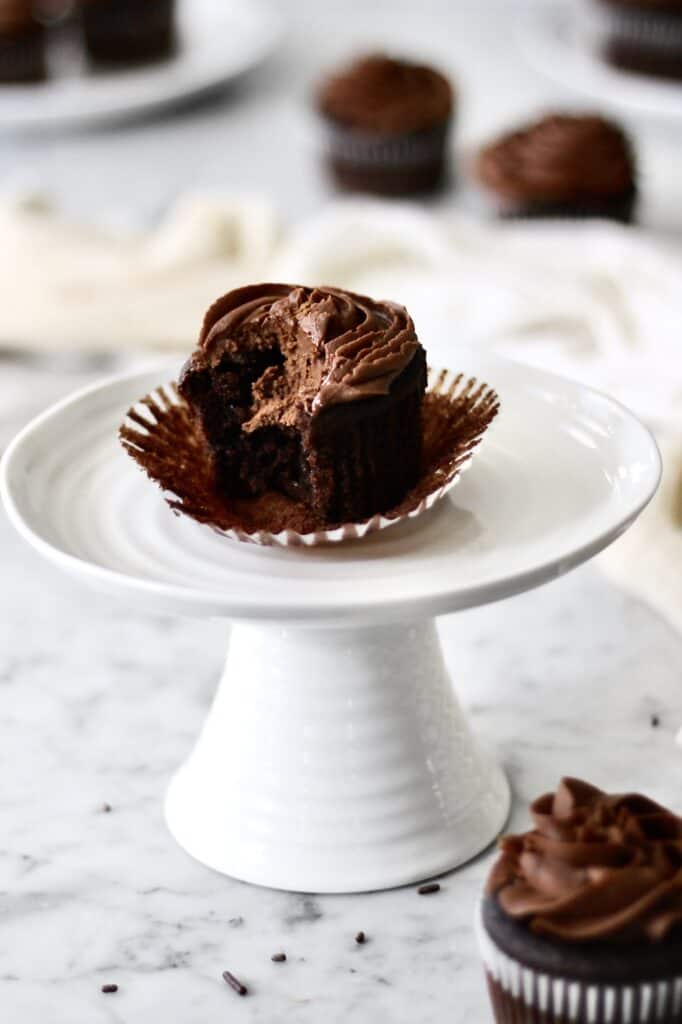 chocolate cupcake with a bite missing from it on a white cake stand
