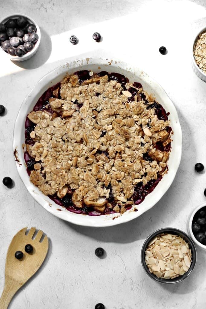 blueberry pear crisp, surrounded by berries and ramekins filled with ingredients for this dessert
