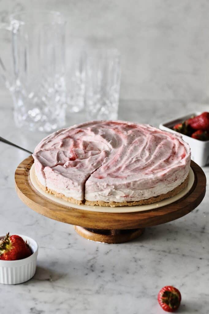 mascarpone strawberry cheesecake, sitting on a brown cake stand with cake server underneath one of three slices