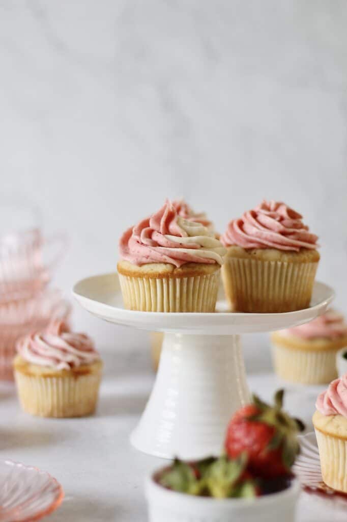 strawberry filled cupcakes sitting on a small white cake stand, decorated with marbled strawberry cream cheese frosting