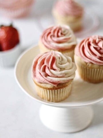 three strawberry filled cupcakes on a white cake stand