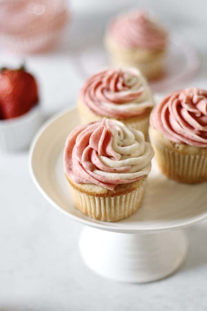 three strawberry filled cupcakes on a white cake stand