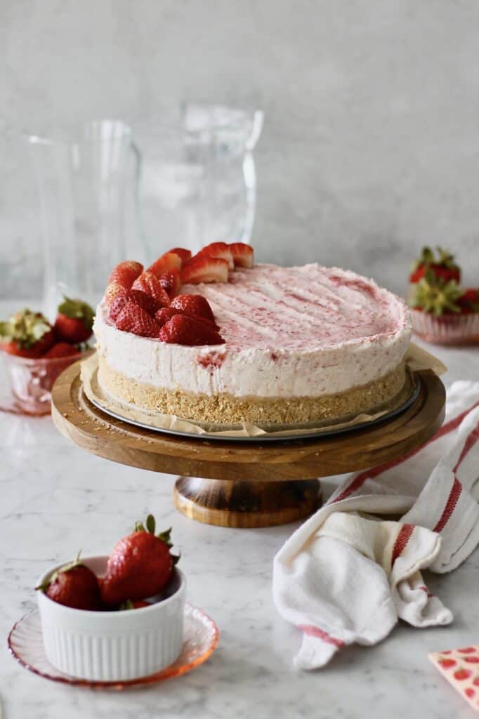 strawberry mascarpone cheesecake sitting on the base of a springform pan on a cake stand, surrounded by strawberries