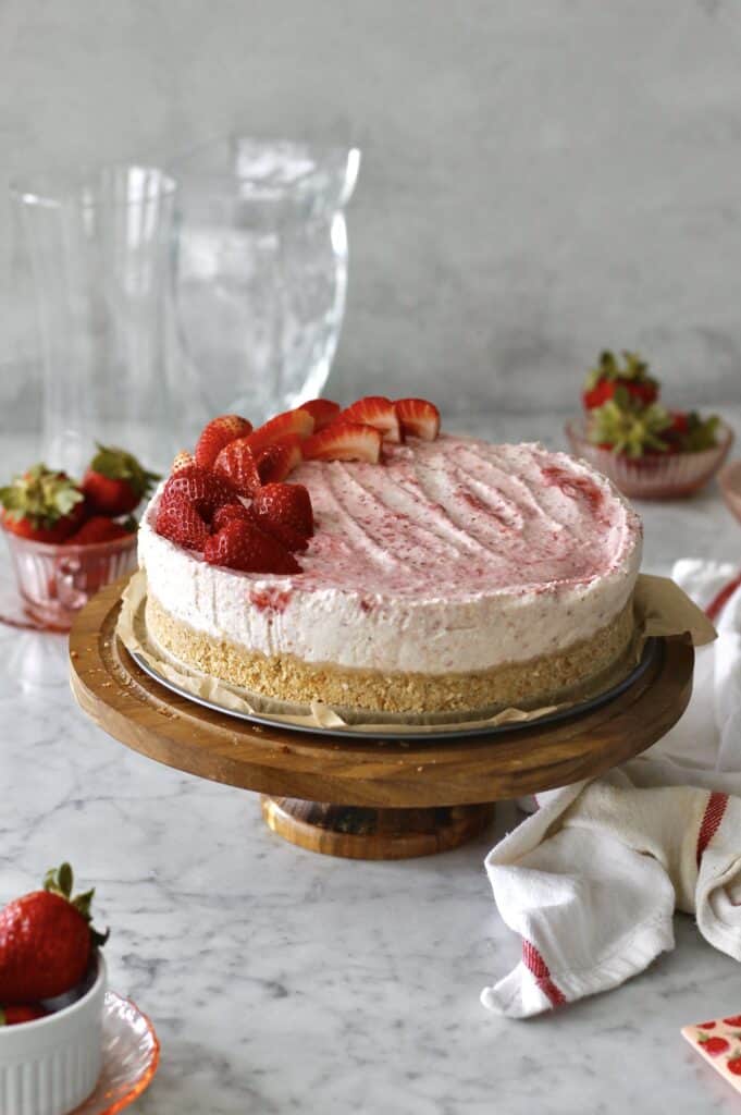 mascarpone strawberry cheesecake, sitting on a brown cake stand with sliced strawberries decorating the top
