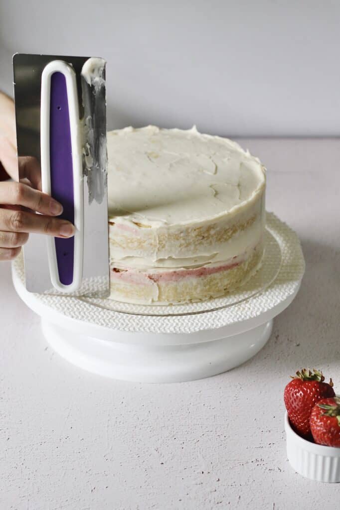 using a cake scraper to finalize frosting on two layer vanilla cake
