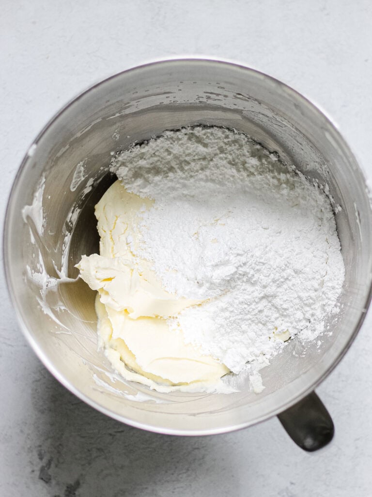 Bowl of ingredients for mascarpone cheesecake recipe, including powdered sugar, heavy cream, and mascarpone, unmixed.