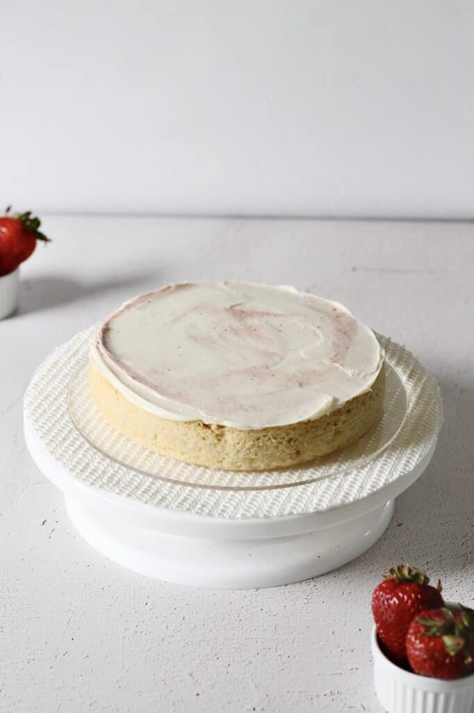 first layer of vanilla cake with strawberry filling, sitting on a cake turntable