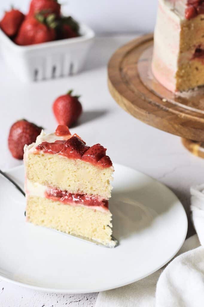 slice of strawberry cake, sitting on a white plate with a cake server underneath it