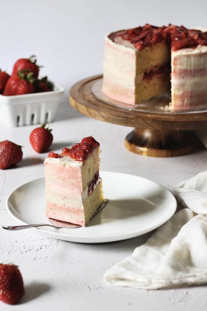 slice of vanilla cake with strawberry filling, pointing backward to the cake, which is sliced and slightly out of focus