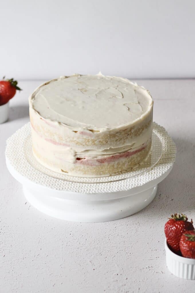 crumb coat of strawberry cream cheese frosting on two layer vanilla cake