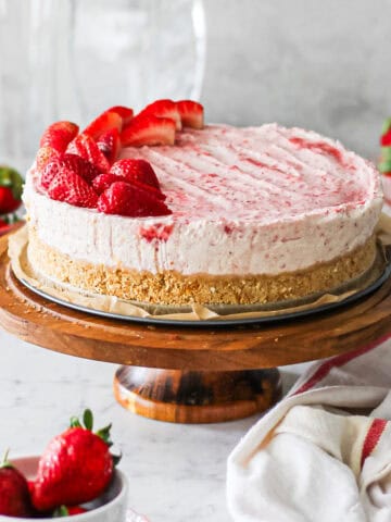 Strawberry mascarpone cheesecake sitting on the base of a springform pan on a cake stand, surrounded by strawberries.