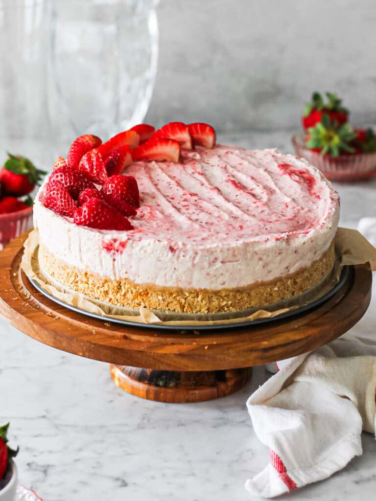 Strawberry mascarpone cheesecake sitting on the base of a springform pan on a cake stand, surrounded by strawberries.