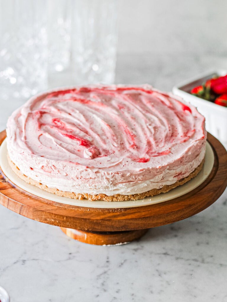 Mascarpone strawberry cheesecake, sitting on a brown cake stand.