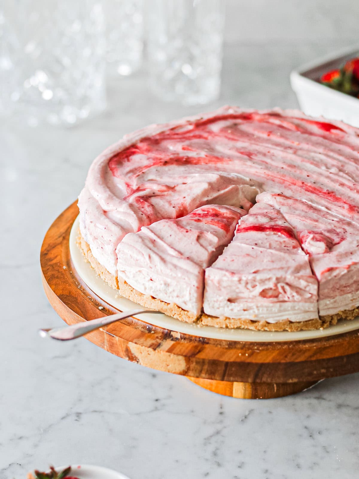 Mascarpone strawberry cheesecake, sitting on a brown cake stand with cake server underneath one of three slices.