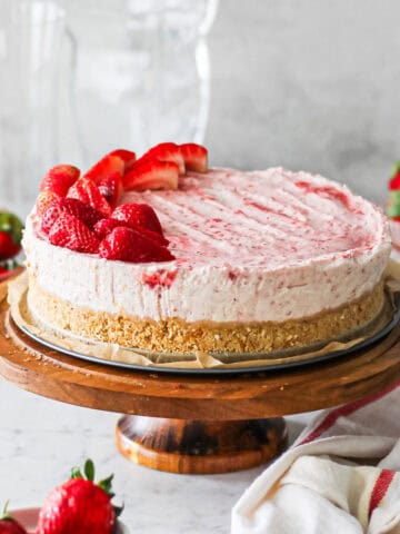 Strawberry mascarpone cheesecake sitting on the base of a springform pan on a cake stand, surrounded by strawberries.